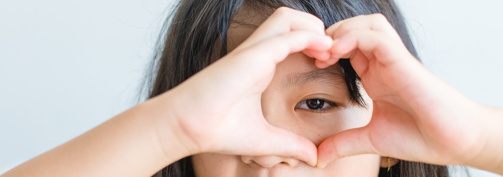 asian girl signing a heart over her eye